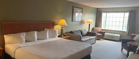 A hotel room with a large bed, a sofa, a chair, a desk, and a window with curtains.