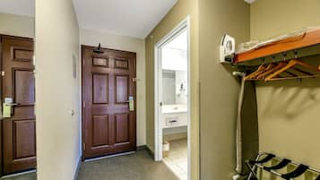 A hotel room with a wooden door, a coat rack, and a bathroom visible through an open door.