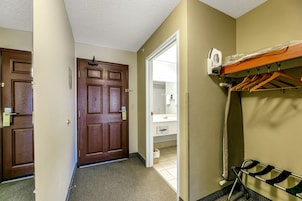 Una habitación de hotel con una puerta de madera, un perchero y un baño visible a través de una puerta abierta.