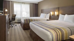 Ein Hotelzimmer mit zwei Betten, einem Schreibtisch, einem Stuhl und einem fenster mit Vorhängen.