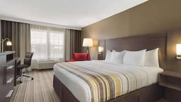 A hotel room with a large bed, a desk, a chair, and a window with curtains.
