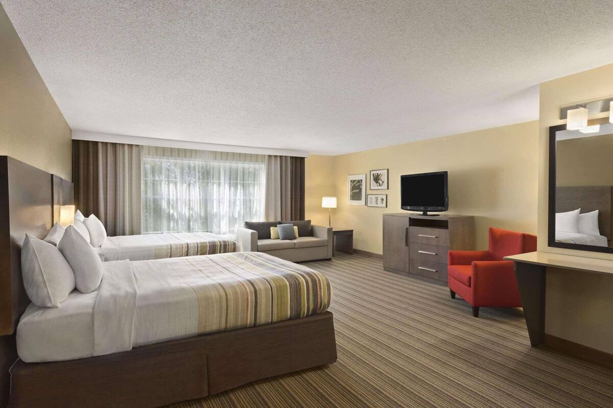 A hotel room with two beds, a desk, a television, and a mirror.
