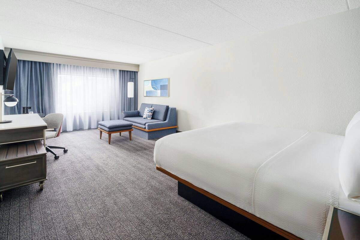 Ein Hotelzimmer mit einem großen Bett, einem Schreibtisch mit Stuhl, einem kleinen Tisch und einer Couch.