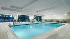 A modern indoor swimming pool with clear blue water, surrounded by tiled flooring and equipped with multiple lounge chairs and tables. - Courtyard by Marriott Chicago Midway Airport (Chicago)