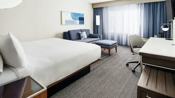 A hotel room with a large bed, a desk, a chair, and a sofa.