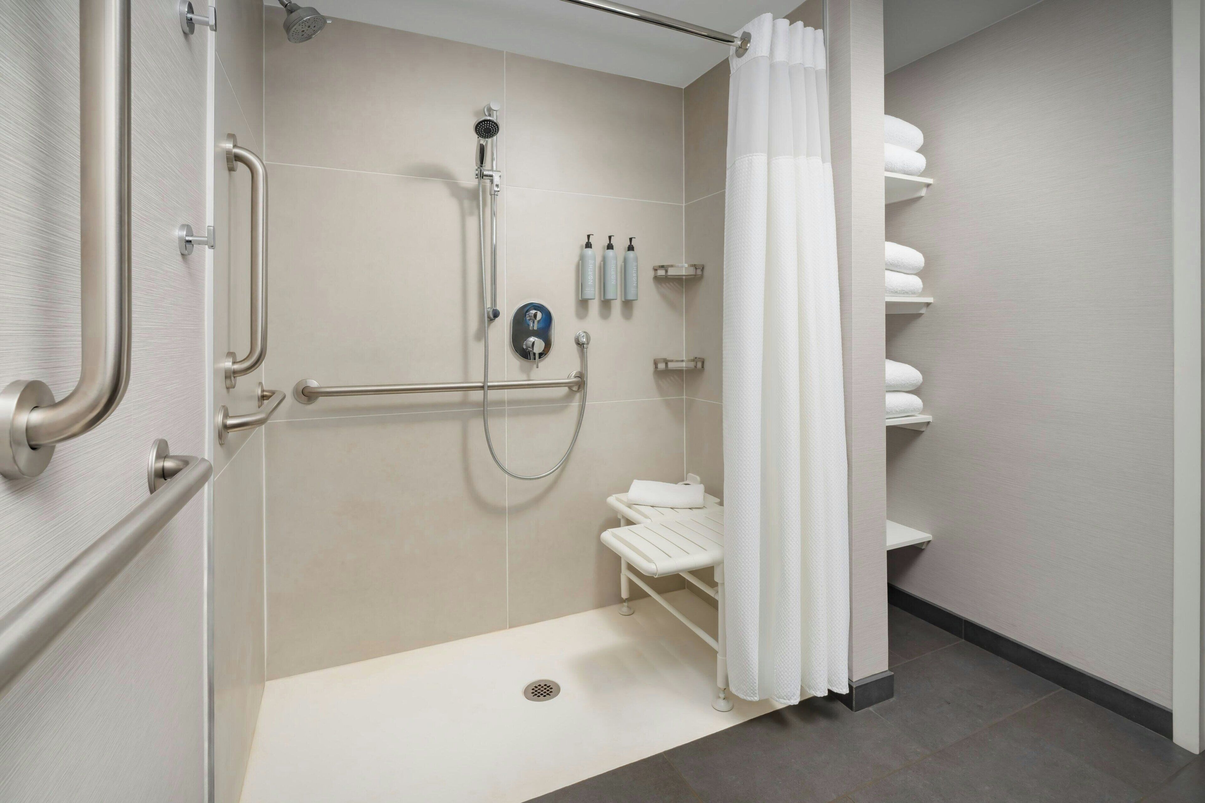 A modern bathroom with a walk-in shower, grab bars, a white sink, and a towel rack.