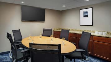 A conference room with a round table, six chairs, a projector screen, and a framed picture on the wall.