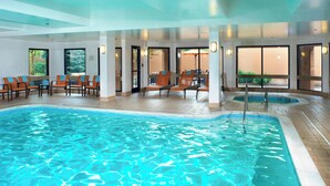 An indoor swimming pool with clear water, surrounded by seating areas and large windows. - Courtyard by Marriott Cleveland Airport North (North Olmsted)