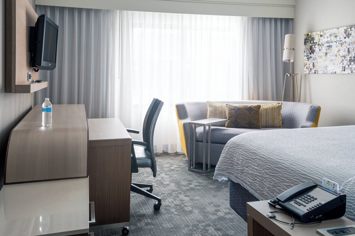 Une chambre d’hôtel équipée d’un lit, d’un bureau, d’une chaise, d’une télévision, d’une lampe et d’un téléphone.