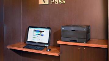 A desk with a laptop and a printer, a sign reading "Boarding Pass", and a wooden shelf.