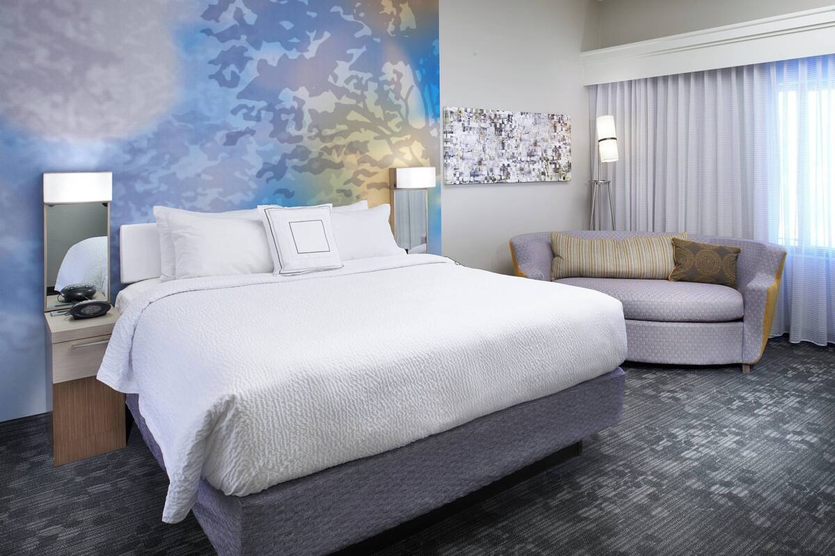 Ein Hotelzimmer mit einem großen Bett, einer Couch, einem Nachttisch mit Lampe und einer Wand mit Tarnmuster.