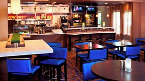A hotel bar with multiple seating areas, a bar counter, and a television screen. - Courtyard by Marriott Cleveland Airport North (North Olmsted)