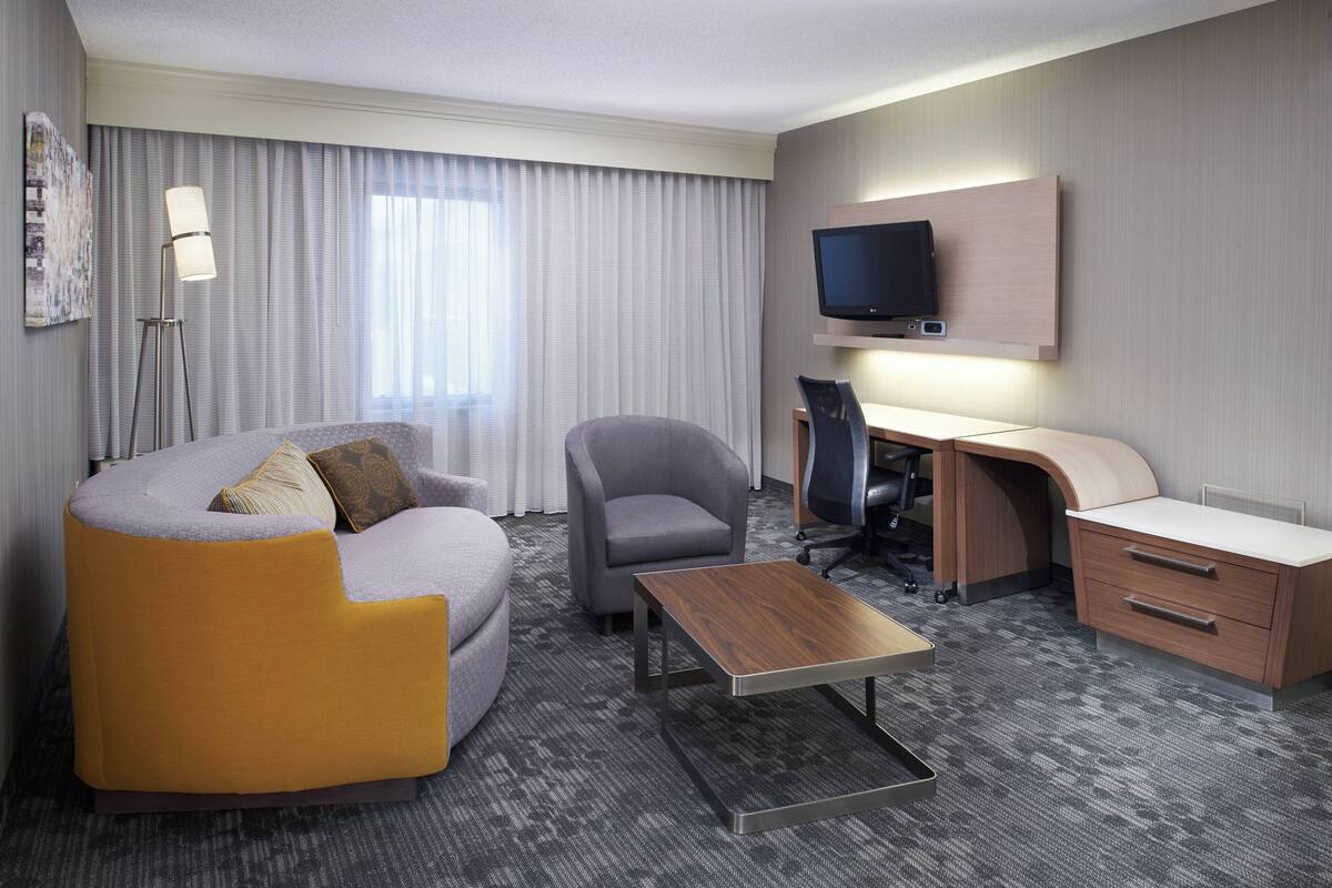 Ein modernes Hotelzimmer mit Sofa, Ohrensessel, Schreibtisch und Fernseher.