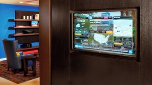 A hotel reception area with a digital display showing the time and weather, a seating area with a chair and a small table, and a blue wall. - Courtyard by Marriott Cleveland Airport North (North Olmsted)