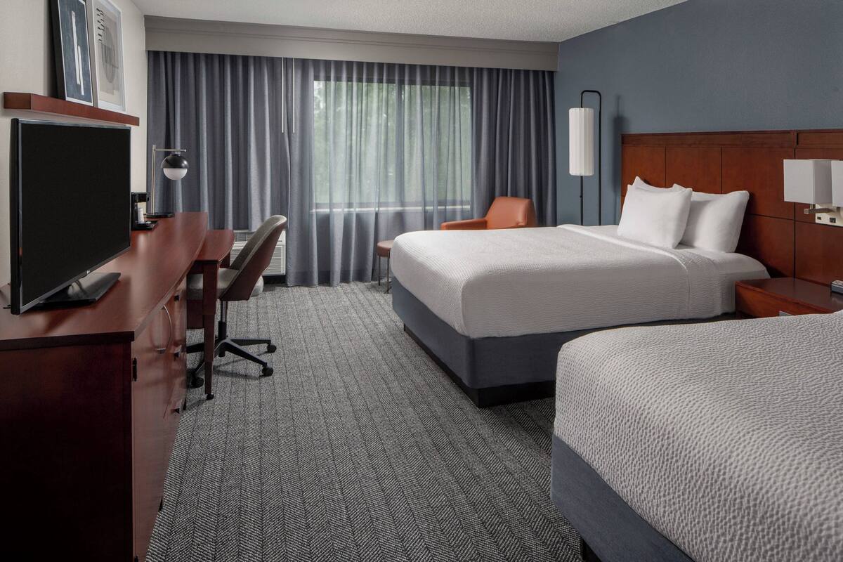 A hotel room with a large bed, a desk with a chair, a television, and a window with curtains.