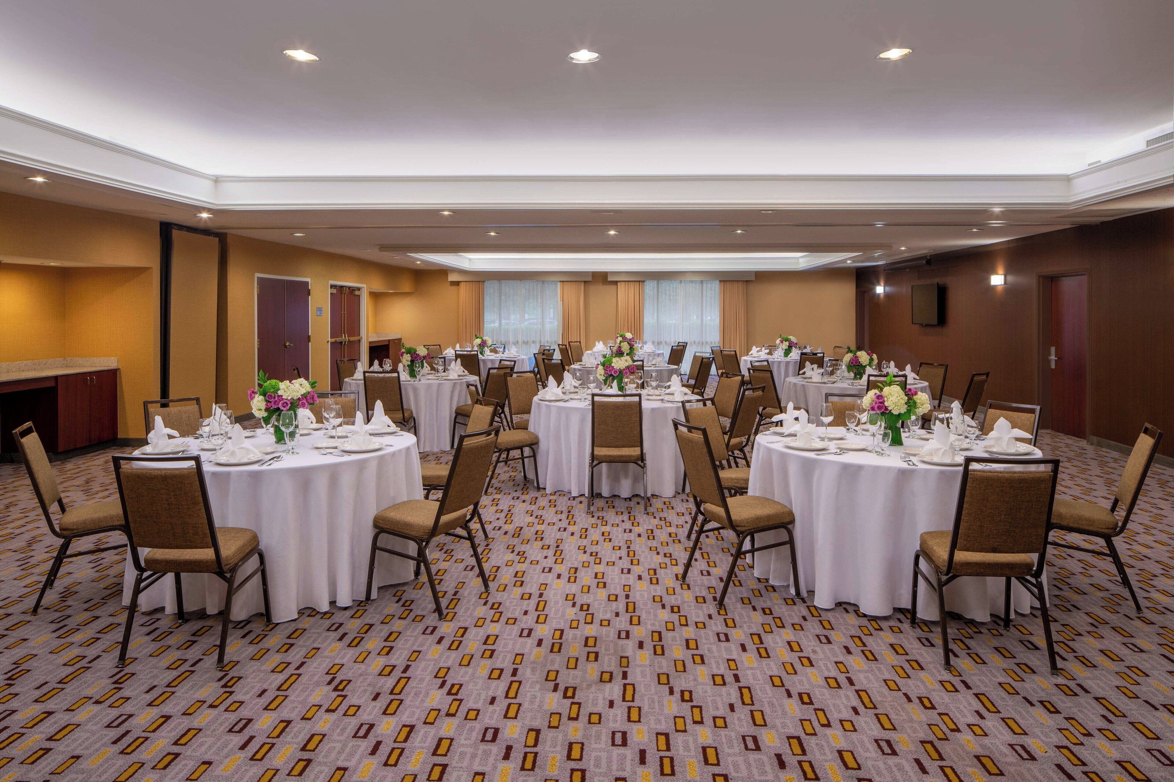 A large conference room with multiple round tables, each set with white tablecloths, chairs, and floral centerpieces.