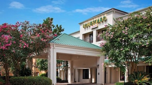 A hotel entrance with a covered walkway, clear signage, and lush landscaping. - Courtyard by Marriott New Orleans Covington/Mandeville (Covington)