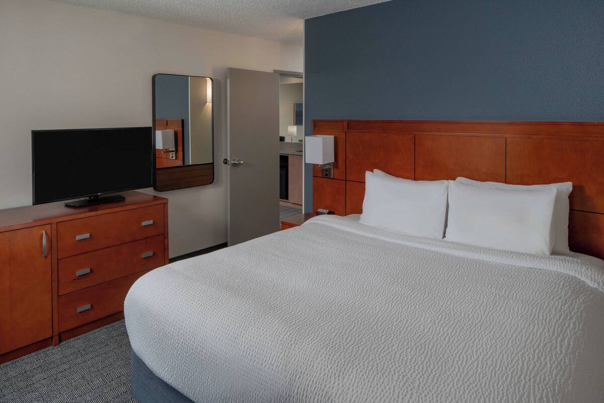 A hotel room with a large bed, a TV on a wooden dresser, a mirror, and a wooden headboard.