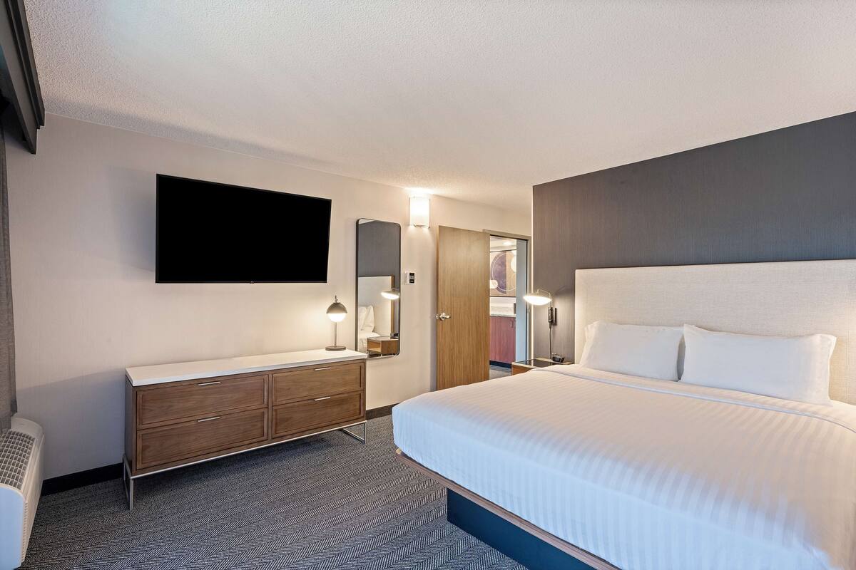 A hotel room with a large bed, a flat-screen TV mounted on the wall, a wooden dresser, and a mirror.
