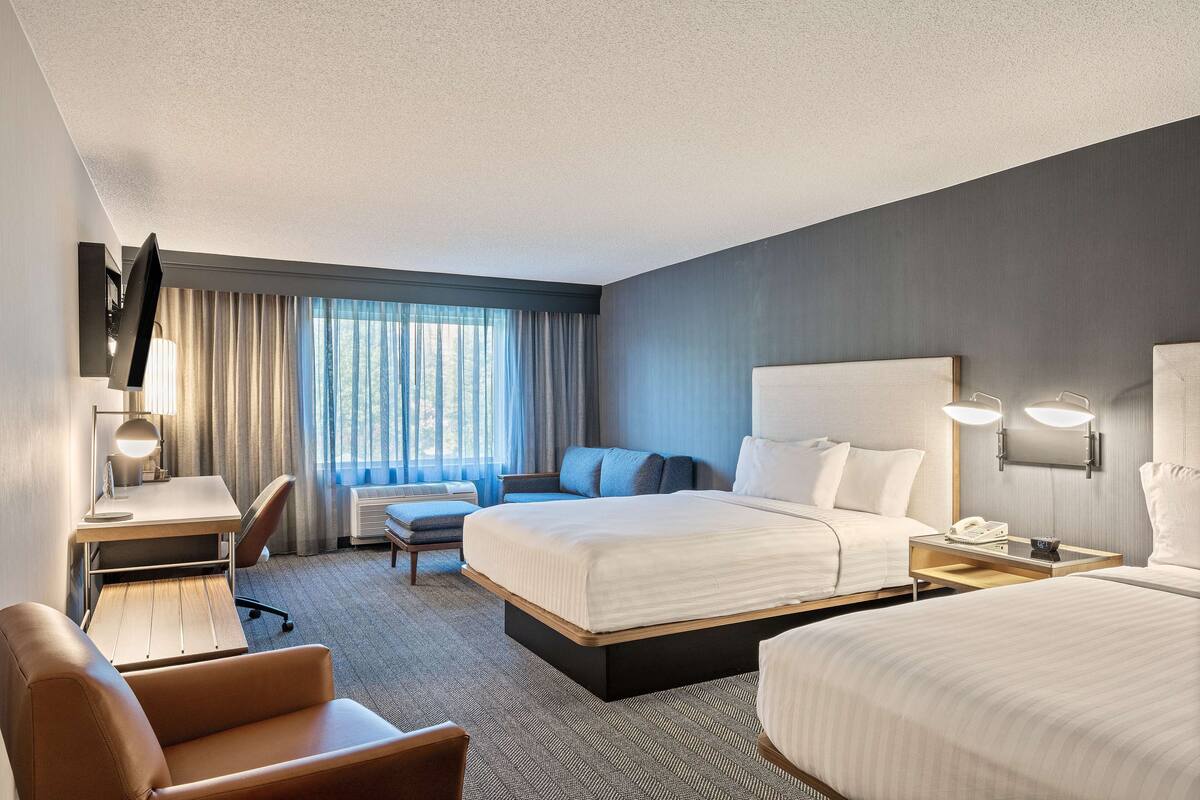 A hotel room with a large bed, a desk with a lamp, a chair, and a bedside table with a phone.
