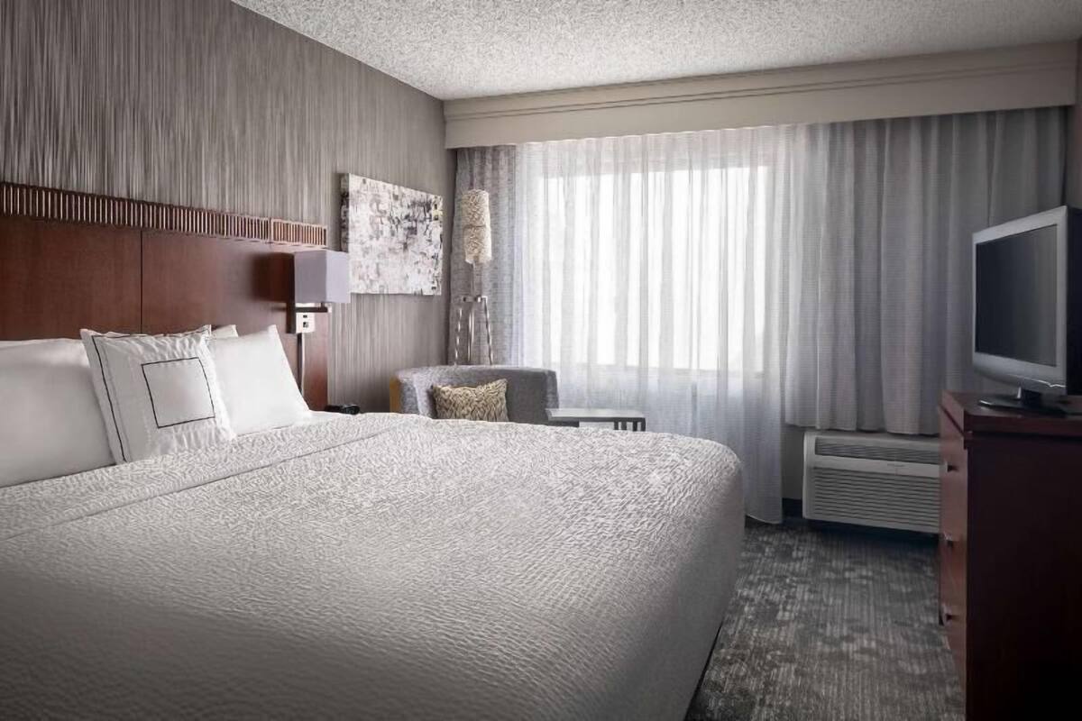 A hotel room with a large bed, a television, a chair, and a desk.