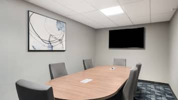 A conference room with a wooden table, six chairs, a flat-screen TV, and a large abstract painting on the wall.