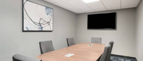 Un salón de conferencias con una mesa de madera, seis sillas, un televisor de pantalla plana y un cuadro abstracto grande en la pared.