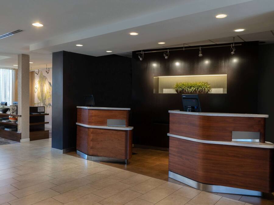 A modern reception area with two wooden reception desks, a dark wall with a recessed light, and a potted plant.