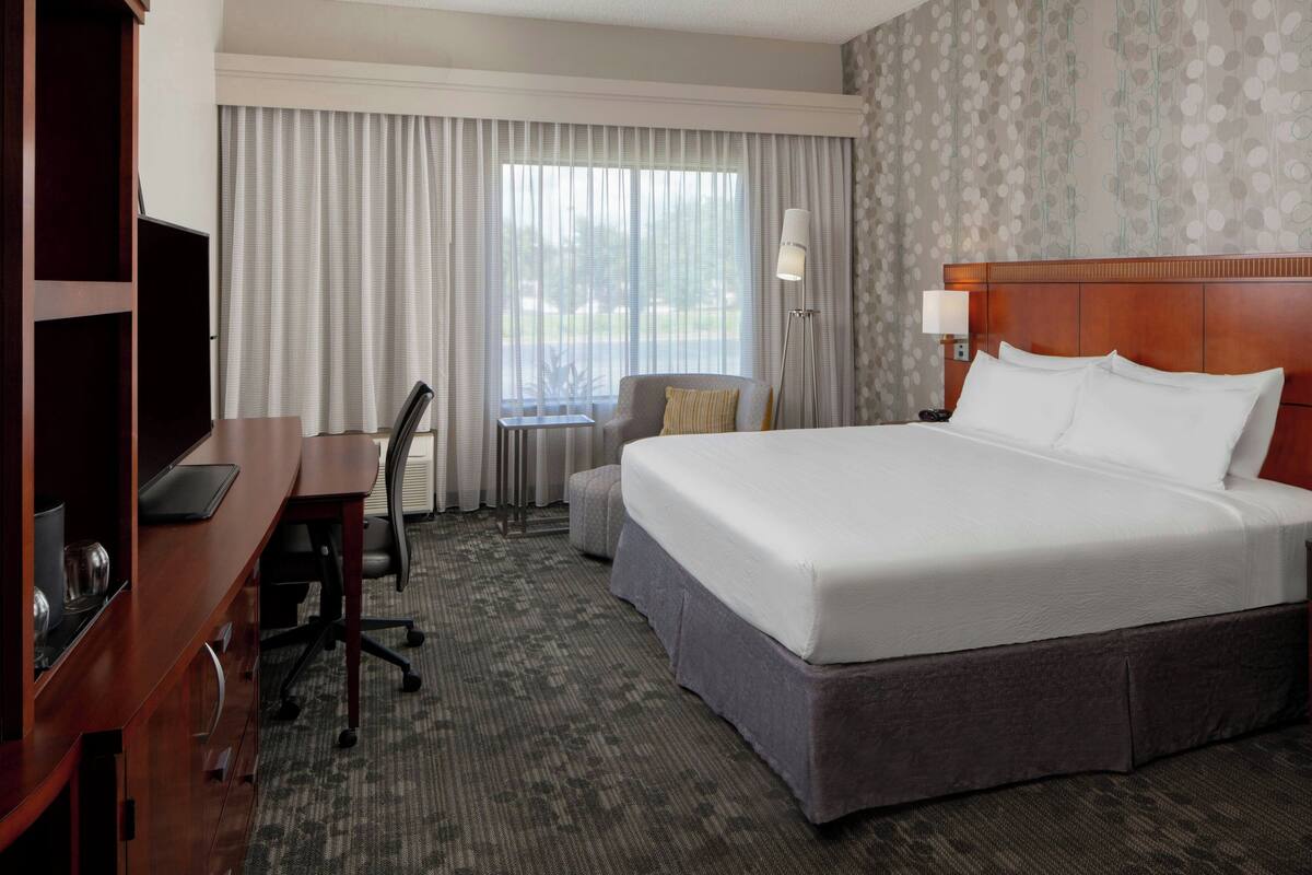 A hotel room with a large bed, a desk with a chair, a small table, and a TV.