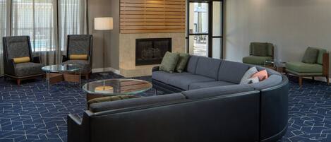 Una sala moderna con un sofá modular, dos sillones, una mesa de centro de vidrio, una chimenea y un ventanal con cortinas.