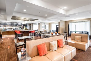 Un moderno vestíbulo de hotel con zona de comedor, asientos y bar.