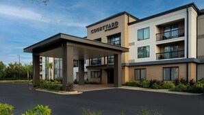 A Courtyard hotel with a covered entrance, multiple balconies, and a landscaped driveway. - Courtyard by Marriott Gulf Shores Craft Farms (Gulf Shores)