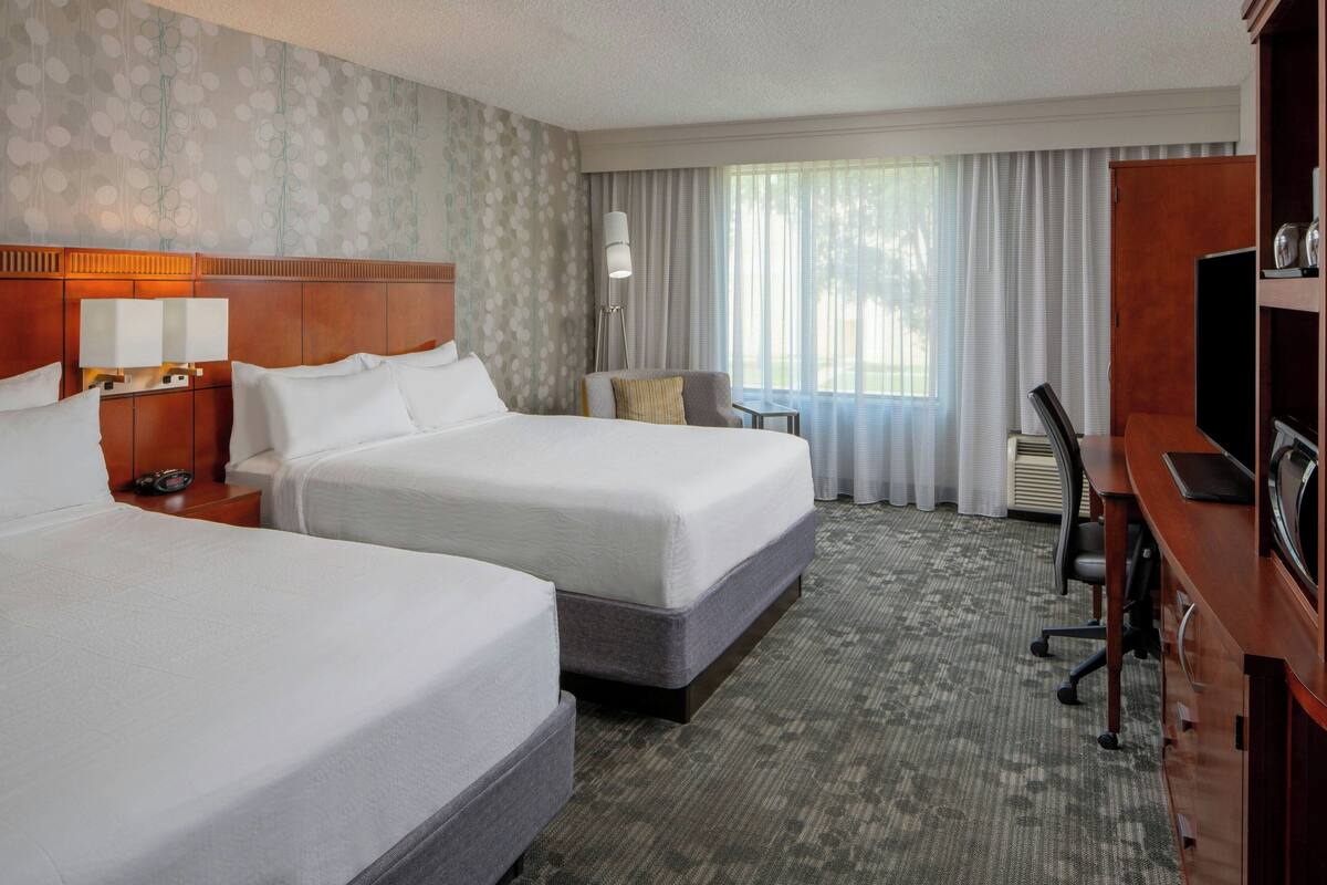 A hotel room with two beds, a desk, a chair, a TV, and a window with curtains.