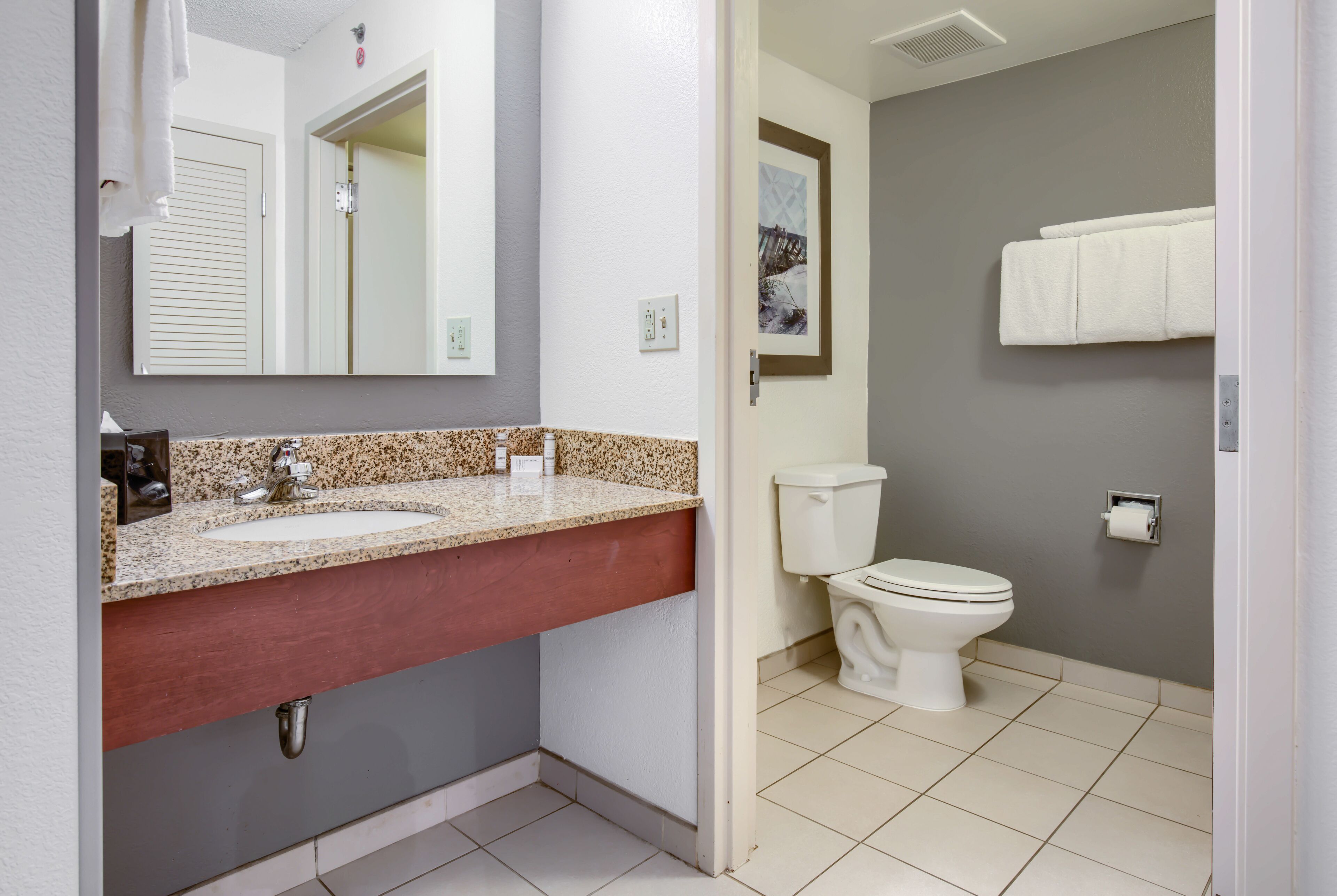 A bathroom with a granite countertop sink, a mirror, a toilet, and a towel rack.