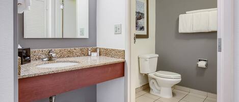 A bathroom with a granite countertop sink, a mirror, a toilet, and a towel rack.