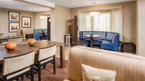 A hotel room with a dining area, a sofa, a small table, and a trash bin. - Courtyard by Marriott Gulf Shores Craft Farms (Gulf Shores)