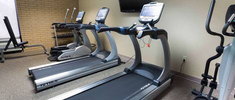 A gym with treadmills, a TV mounted on the wall, and a dumbbell rack.