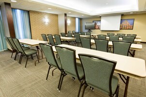 Un salón de conferencias con varias mesas y sillas, una pantalla de proyector y un televisor.