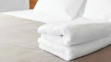 A neatly folded white towel stacked on a bed with a light-colored sheet.