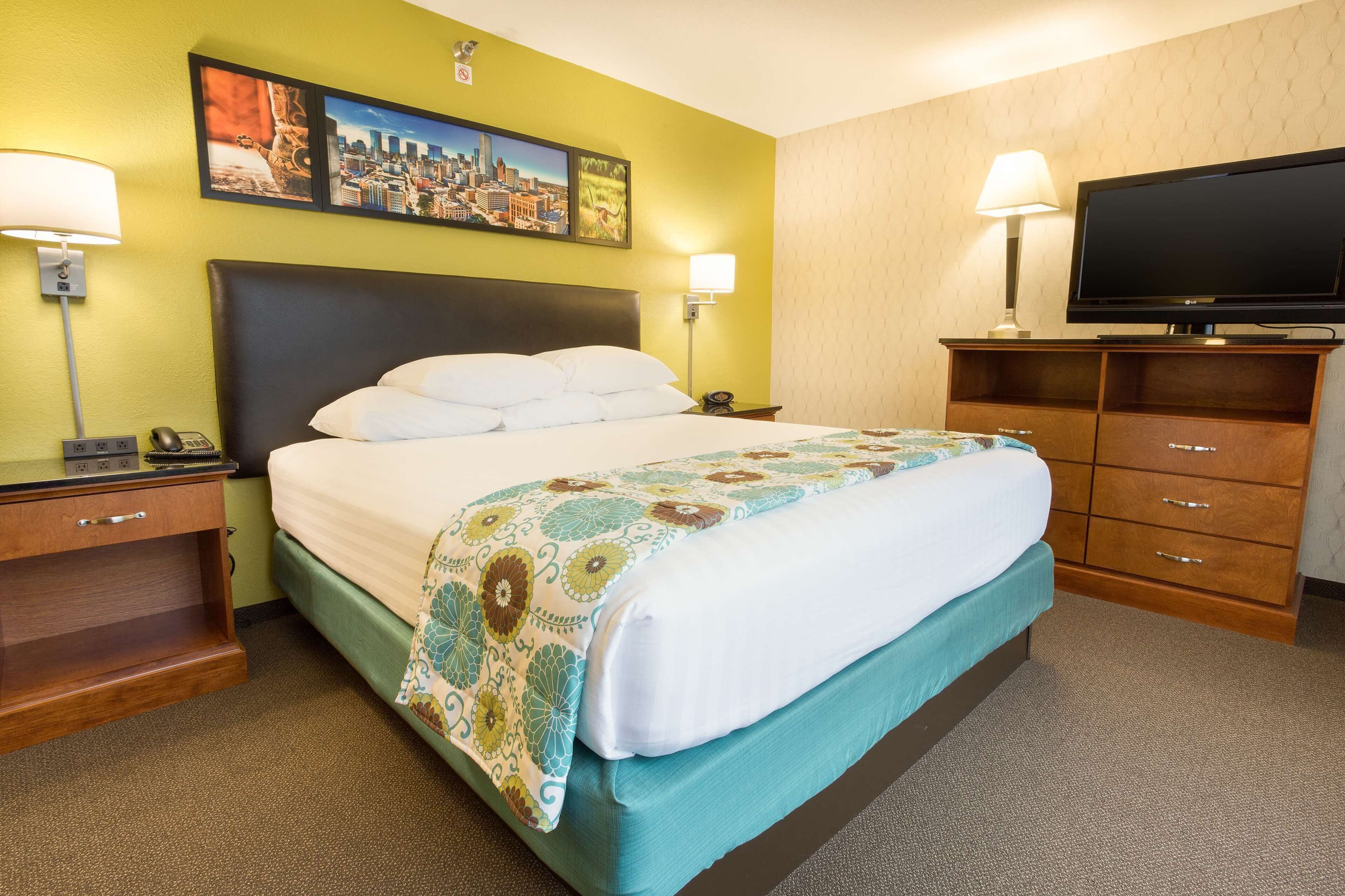 Habitación de hotel con cama, dos mesitas de noche, un televisor y una pared con tres cuadros enmarcados.