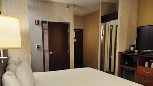 Une chambre d’hôtel avec un grand lit, un bureau avec une lampe, une télévision et un four à micro-ondes.