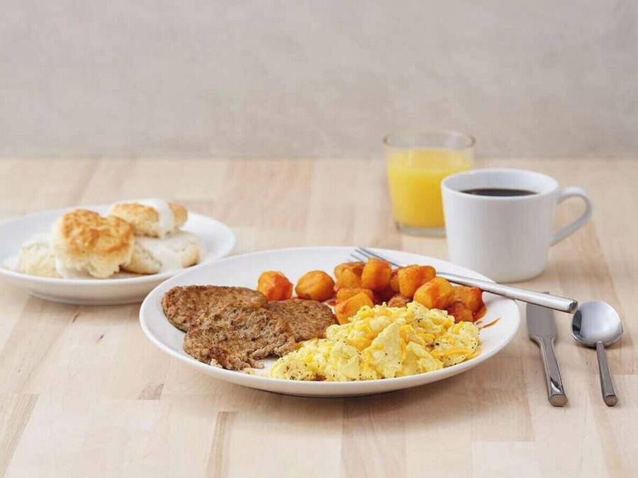 A breakfast setting with two plates of food, a cup of coffee, and a glass of orange juice on a wooden table.