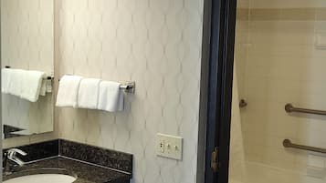 A bathroom with a marble sink, a mirror, two towels on towel racks, a shower with a glass door, and a wall with a subtle pattern.