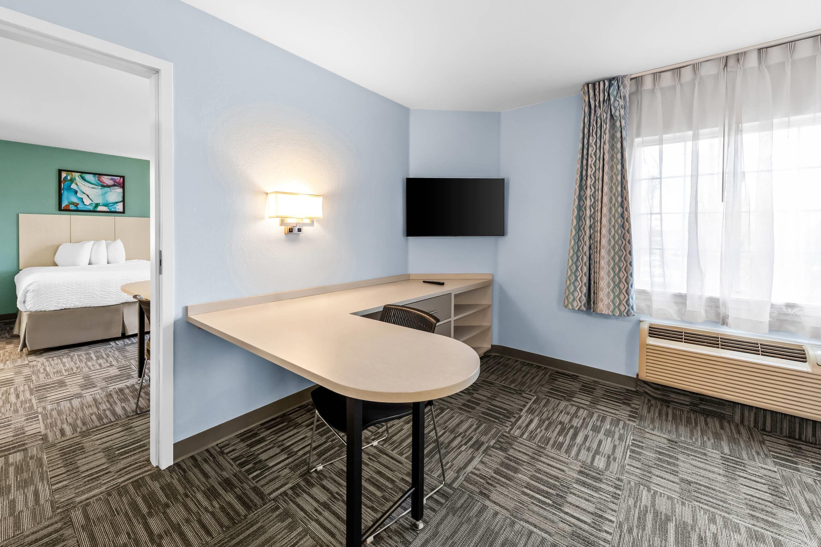 Une chambre d’hôtel équipée d’un lit, d’un bureau, d’un téléviseur à écran plat, d’une fenêtre avec des rideaux et d’un climatiseur fixé au mur.