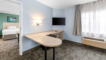 Une chambre d’hôtel équipée d’un lit, d’un bureau, d’un téléviseur à écran plat, d’une fenêtre avec des rideaux et d’un climatiseur fixé au mur.