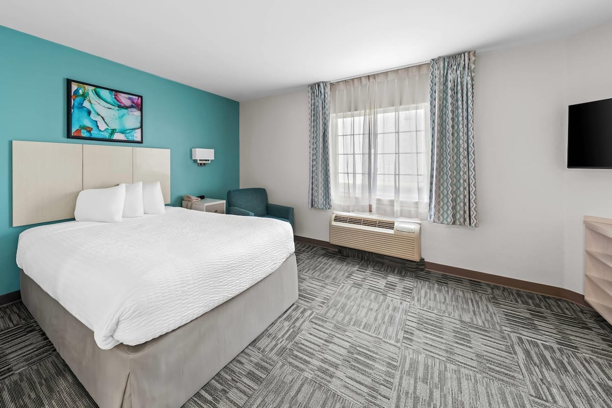 A hotel room with a bed, a desk, a chair, a TV, and a window with curtains.