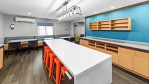 A modern kitchen with a long counter, orange stools, and wooden cabinets. - MainStay Suites Cincinnati Blue Ash (Cincinnati)