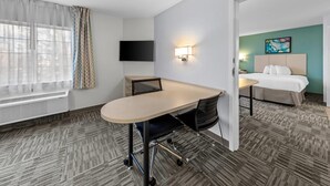 A hotel room with a large desk, a bed, a TV, and a painting on the wall. - MainStay Suites Cincinnati Blue Ash (Cincinnati)
