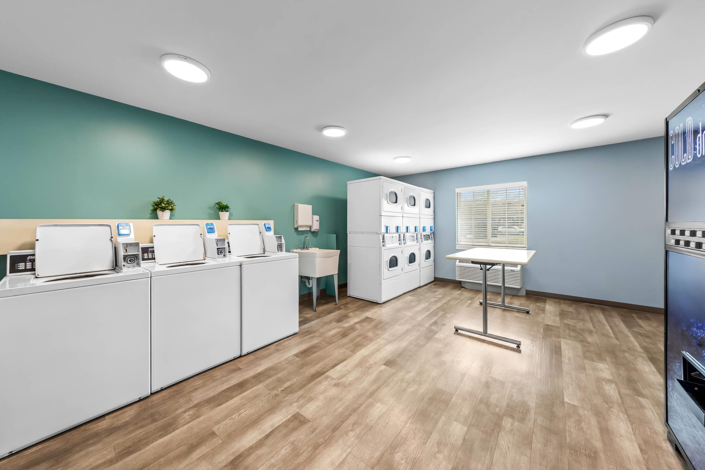 A laundry facility with multiple washing machines, a sink, and a table with a chair.