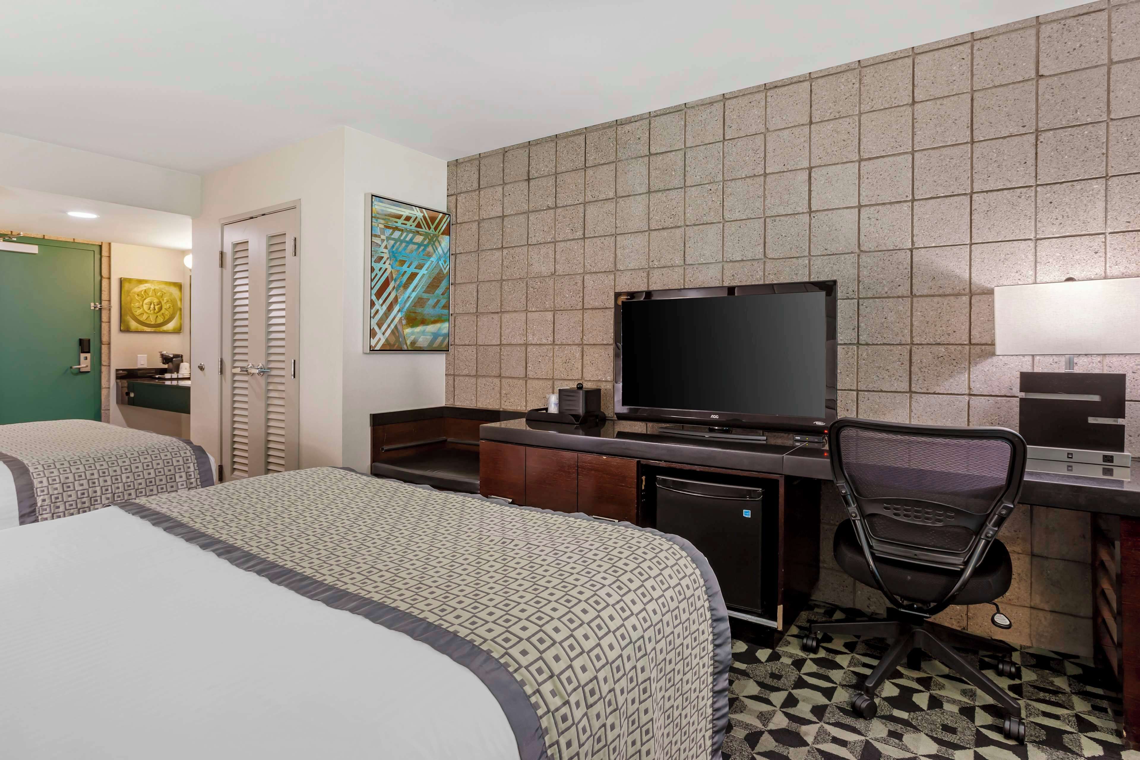 Een hotelkamer met twee bedden, een bureau met een computer, een televisie en een stoel.